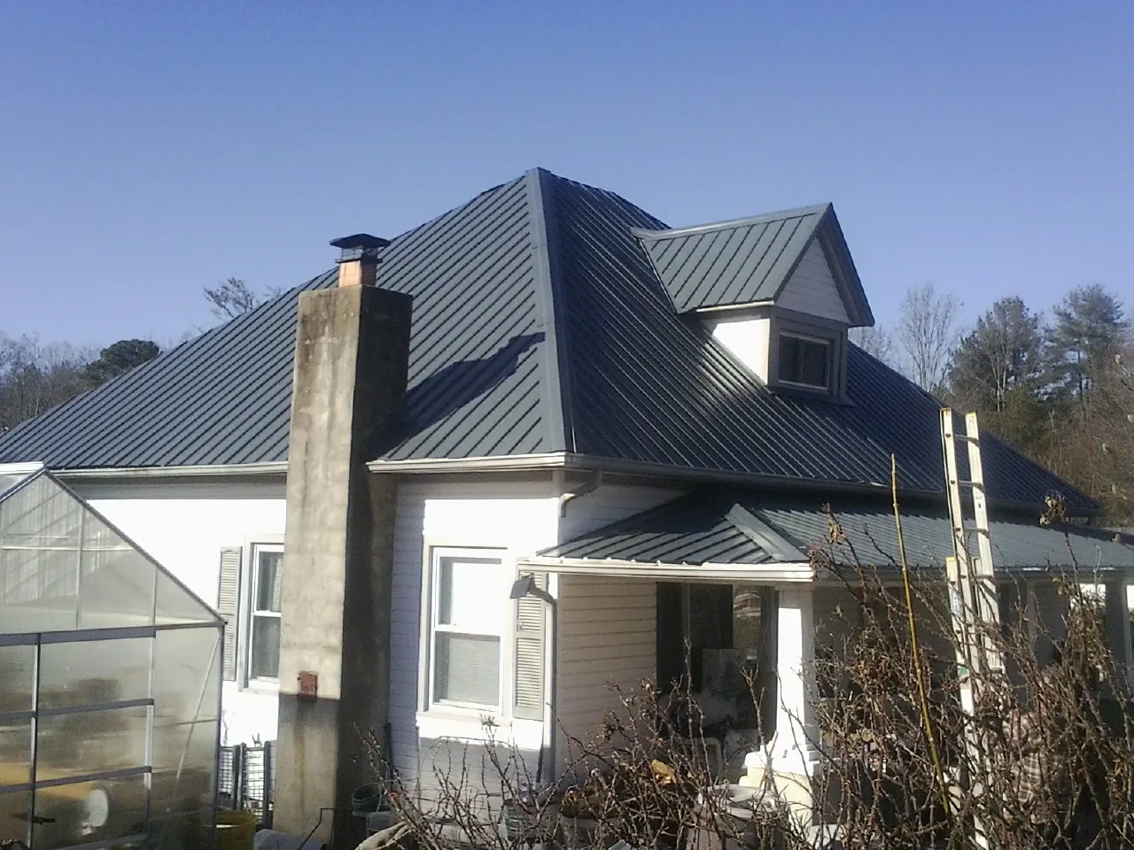 Dark blue standing seam metal roof on a white farmhouse with dormer — Slate & Tile Roof Repair by Roofing Brothers in Horse Creek
