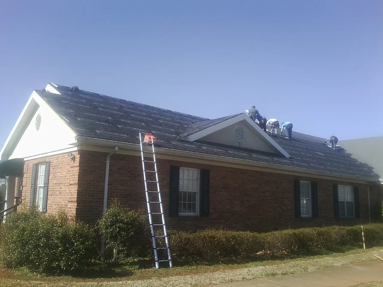 Crew tearing shingles off a brick ranch roof with a ladder set — Metal Roof Repair work by our crew in Horse Creek