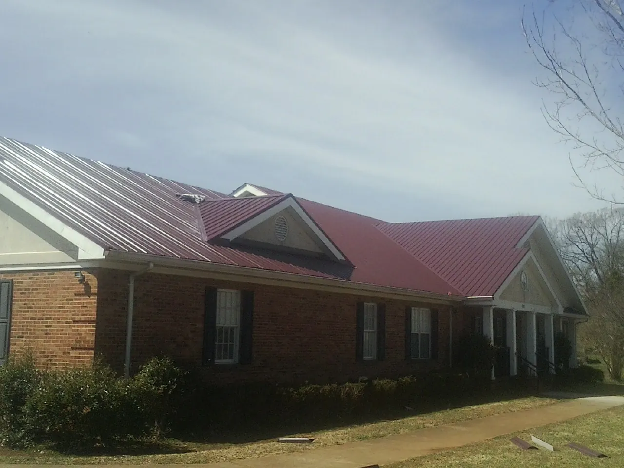 Red metal roof with gabled entries on a long brick building, from a Hail Damage Roof Repair job in Horse Creek