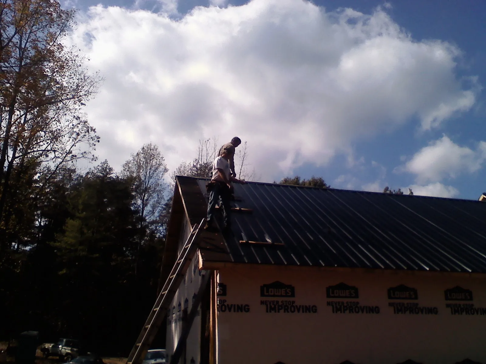 Roofer fastening dark metal panels high against a cloudy sky, from a Roof Inspection job in Horse Creek