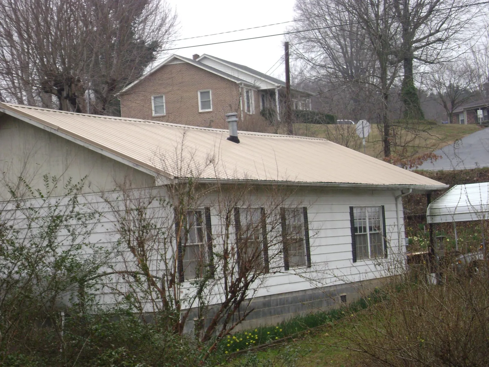 Tan metal roof on a white sided house set into a hillside — Commercial Roofing by Roofing Brothers in Horse Creek