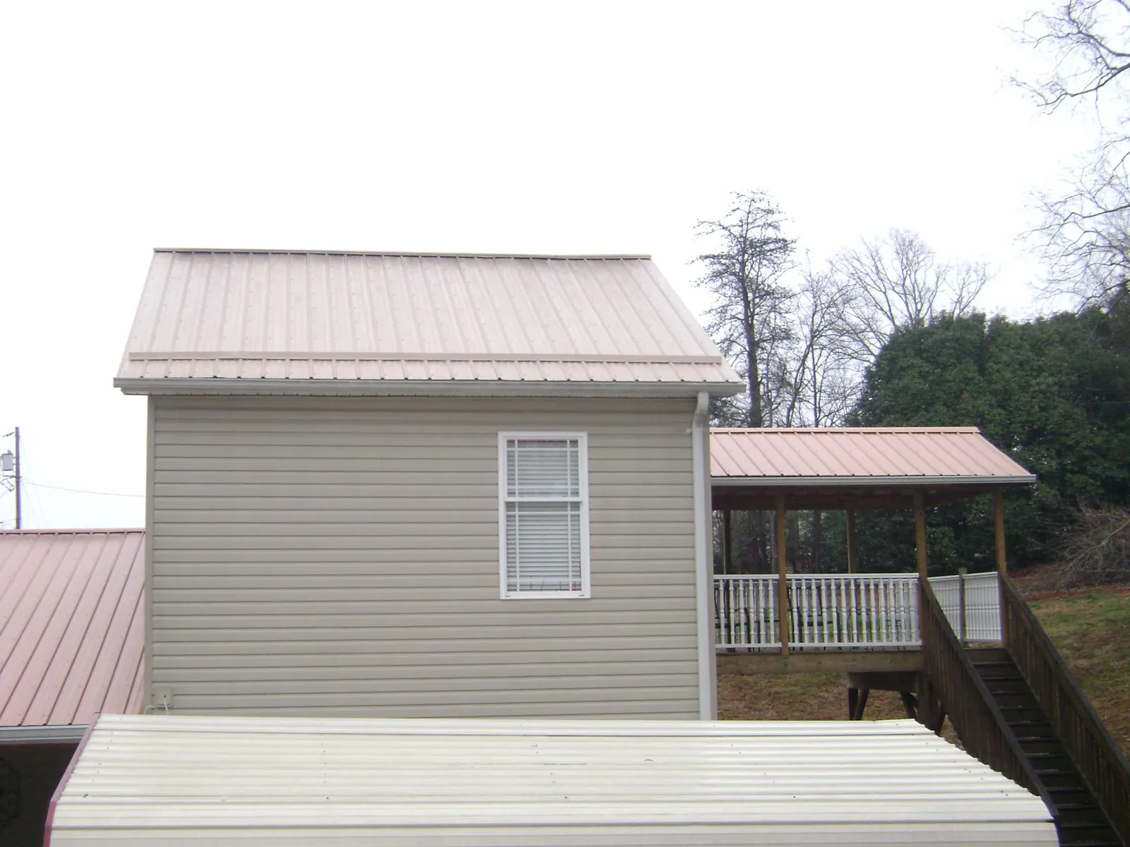 Tan metal roofs on a two story addition and attached porch, from a Roof Replacement job in Horse Creek